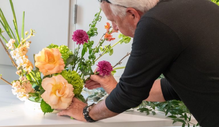 A person in a black shirt, creating a floral design featuring peach and magenta flowers.