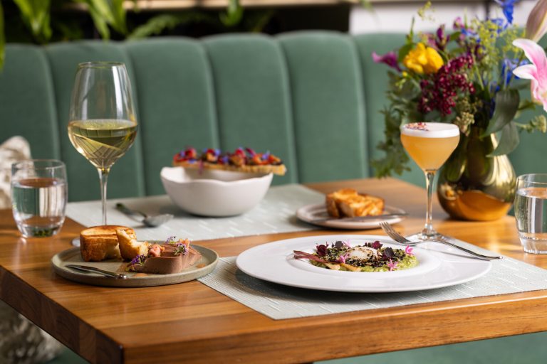 A table in a fine dining restaurant featuring several plates of food, and two wine type glasses.