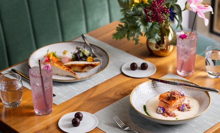A table in a fine dining restaurant featuring several plates of food and a vase of flowers. 