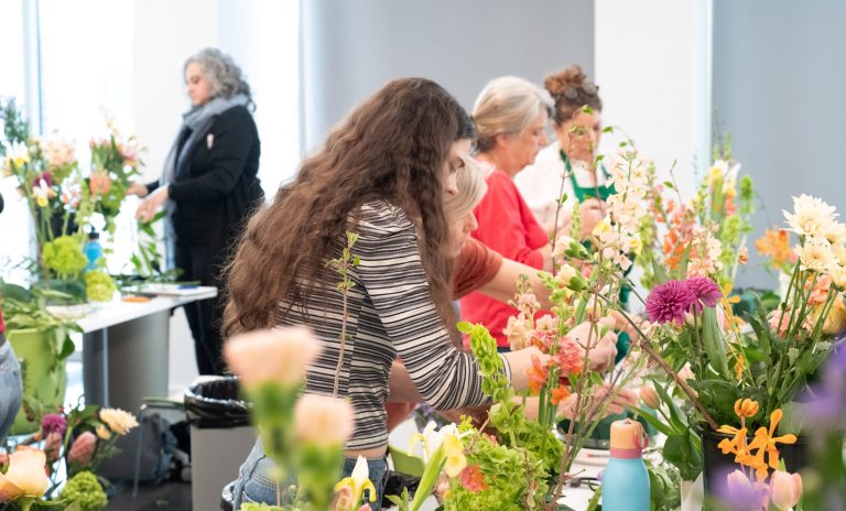 A classroom image of people working at tables crafting floral arrangements.