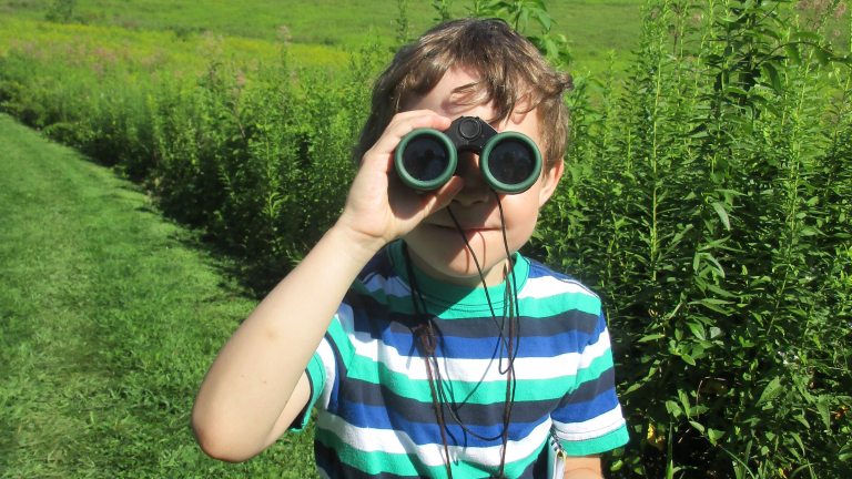 Boy in the Meadow Garden with binoculars on his eyes facing the camera 