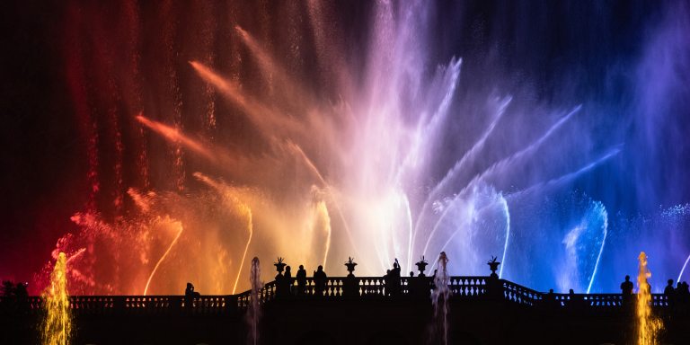 Large fountain jets reach for the night sky, lit in red, white, and blue lights.