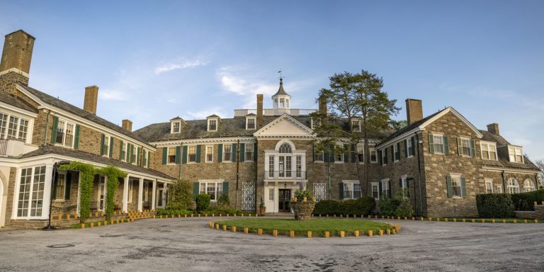 A very large stone estate with brown stone, cream trim, set against a bright blue sky. 