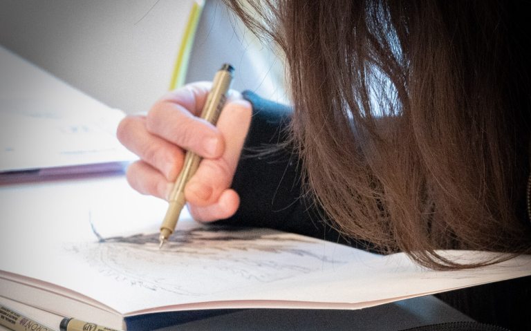 A person with their head bent down, drawing in a sketchbook. 