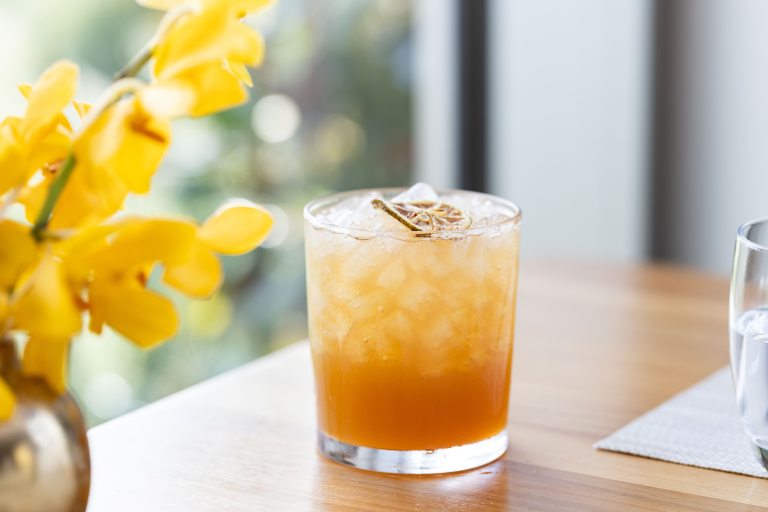 A autumn inspired cocktail in a highball glass, on a light wood table. 