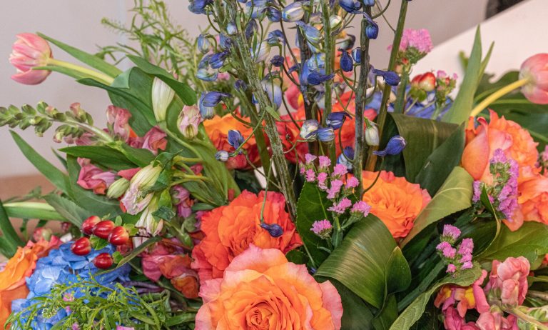 A close up of a vibrant floral arrangement featuring peach roses along with other flower and fliage types.