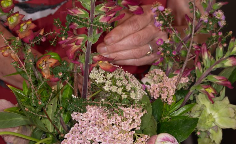 An upclose image of a person's hand arranging stems in a floral arrangement.