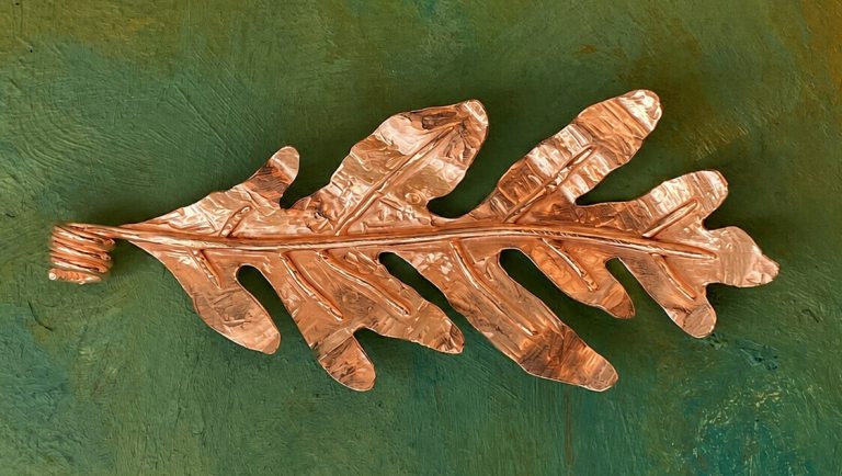 One leaf made out of copper on a green background
