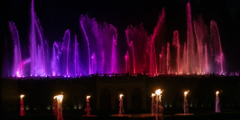 Fountain jets in pink, purple, red, and orange hues, with flames in foreground.
