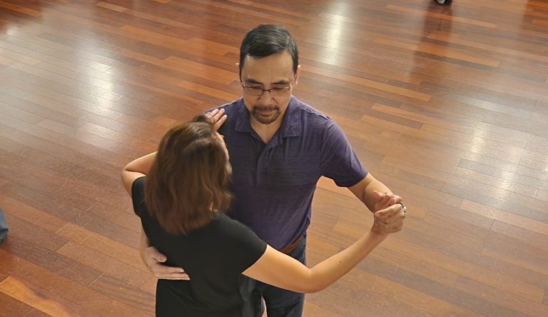 Two people ballroom dancing on a wooden floor.