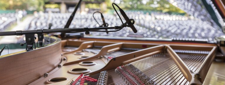 Closeup of a piano opened to show strings, with empty outdoor audience seats in the background.