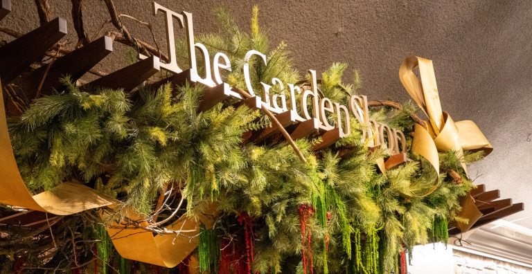 The sign reads The Garden Shop in gold lettering, with holiday foliage draaped around it.