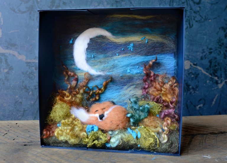 A needle felt shadowbox scene featuring a red fox, a crescent moon, and a green foreground.