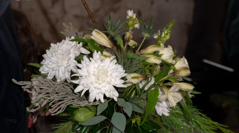 An all white floral arrangement set against a moody dark background.