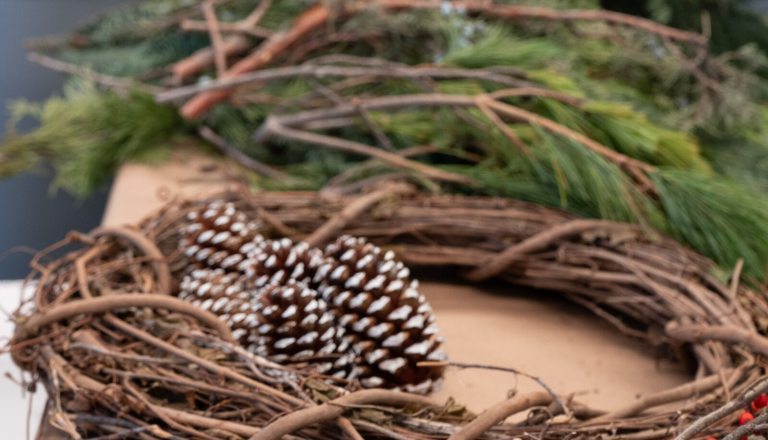 Wreath making materials, including evergreen branches, pinecones, and woven twigs.