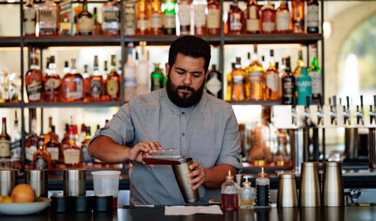 A bartender, mixing a cocktail behind a wood bar. 