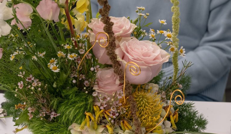 A close up of a floral arrangement featuring light pink roses, yellow foliage, and gold accents. 