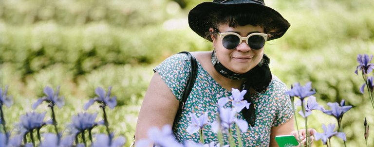 person in sunglasses and hat looking at purple flowers