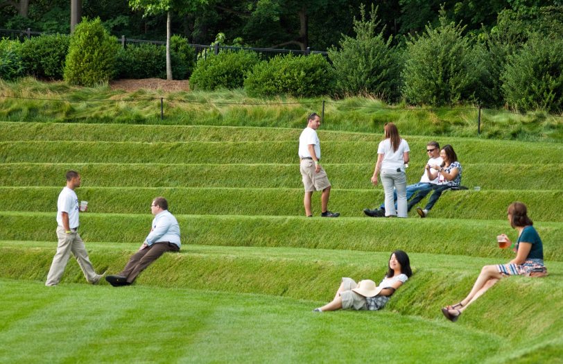 Eight people stand in small groups and alone across levels of green grass