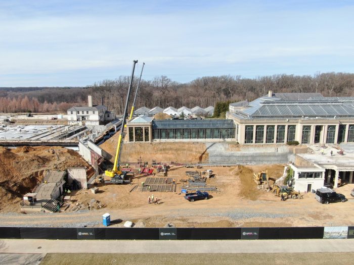 large crane with new construction in left background, and existing greenhouse structure in right background