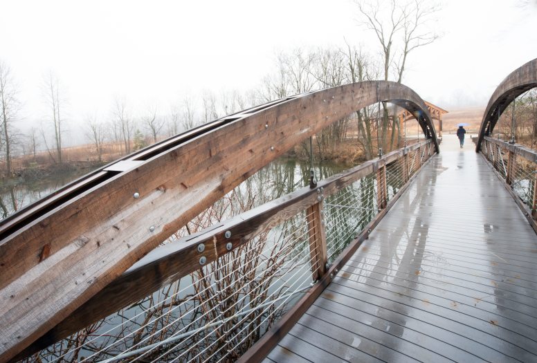 A long bridge over a body of water leads into the distance with a wooden arching side railing