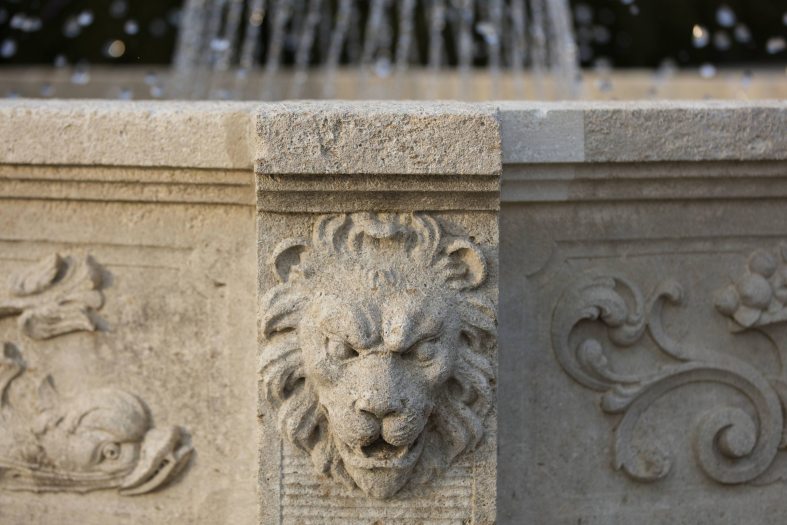 A stone decorative carved lion head adorns a stone fountain structure