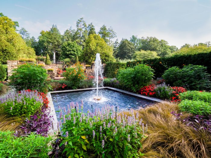 A square fountain surrounded by blooming, lush green and colorful plants