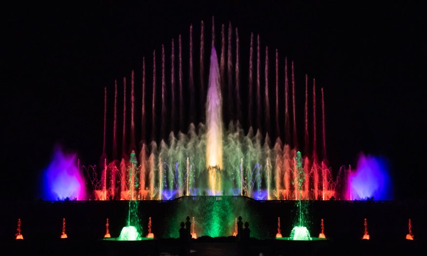 Water from fountains shoots into the air and is illuminated in many colors at night