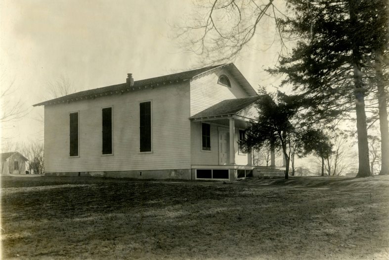 black & white image of a simple white structure with tall windows and peaked roof