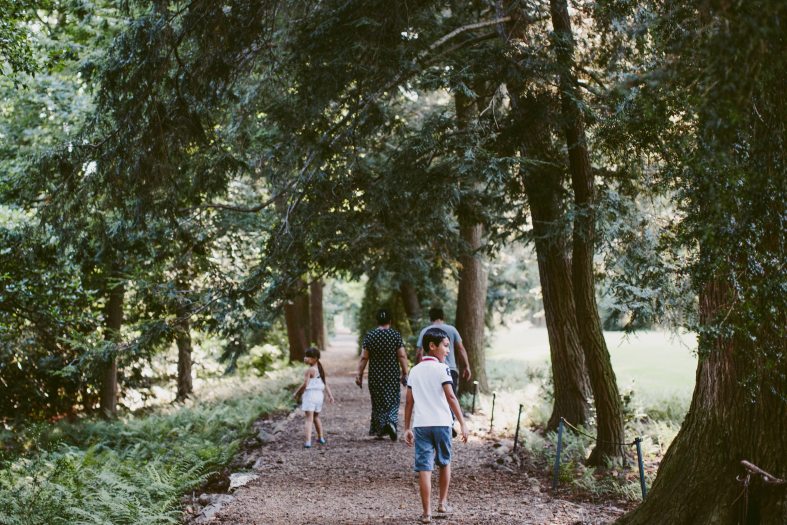 An adult and two children run along a wood chip path lines by large trees