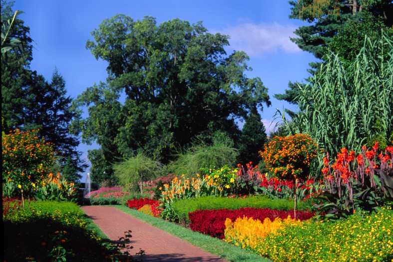 Colorful flower beds line a brick walkway under a blue sky