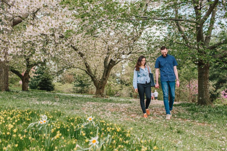 A couple walks along a grass path among flowering trees and geophytes