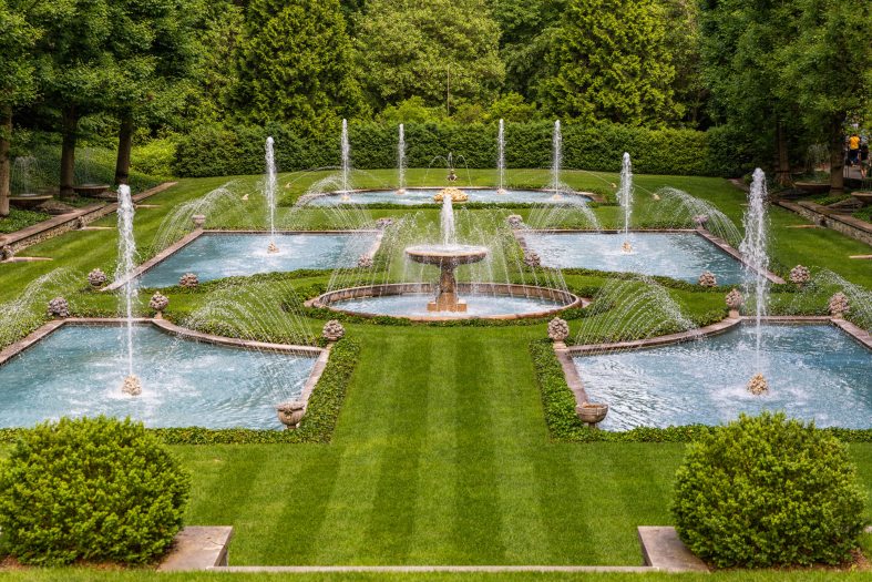 Four rectangular pools of water with fountains in the middle surrounded a small circular fountain with green grass surrounding them all