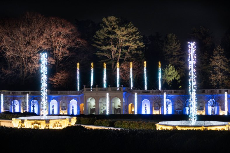 White and blue Christmas lights adorn a stone fountain garden, making the lights look like water