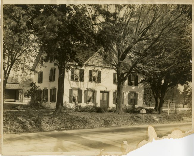 black and white image of an old home with trees in front