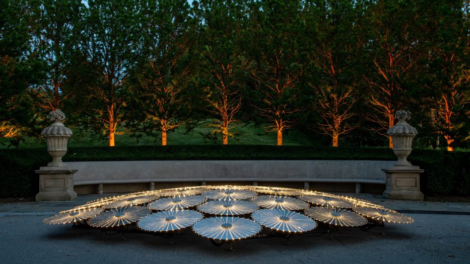 an array of large discs glow along their radial lines, against a backdrop of a curved stone bench and illuminated trees
