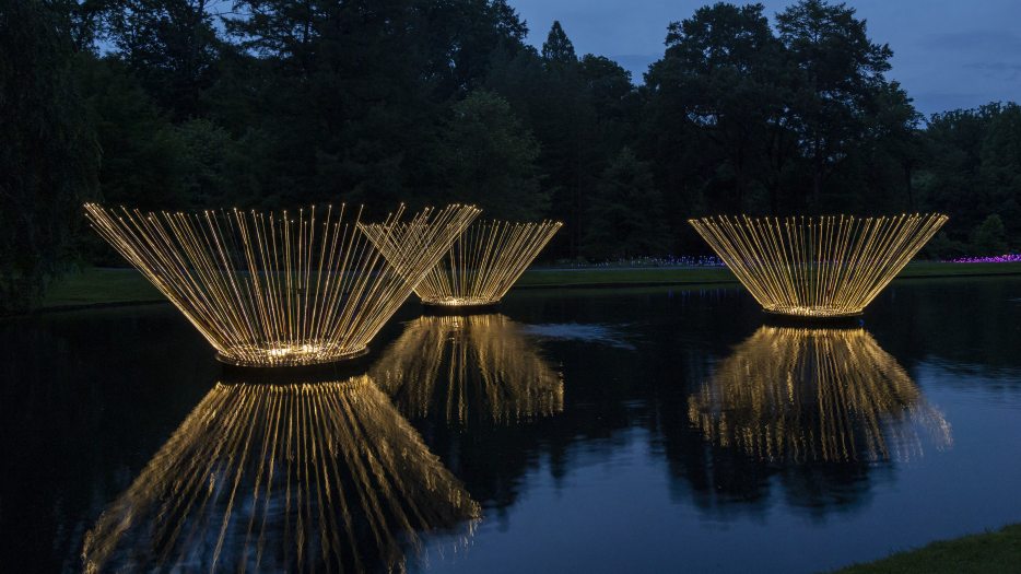 Three large fountains of light rise from the surface of the Small Lake, each fashioned using 100 illuminated fishing rods that cast lines of light against the dark water