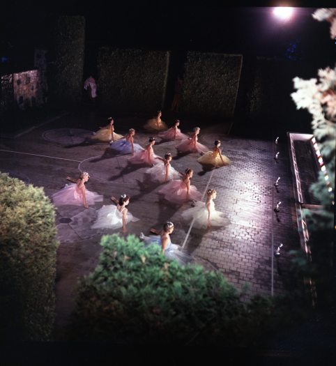 A group of ballerinas perform on stage for an audience under lights during a nighttime show