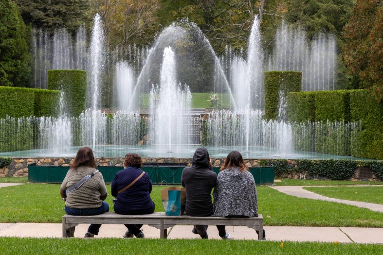 four people sit on a bench in front of fountains on a stage