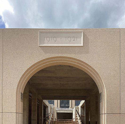 A facade datestone reads "1919-1921", above an arch through which is seen the construction taking place in the background