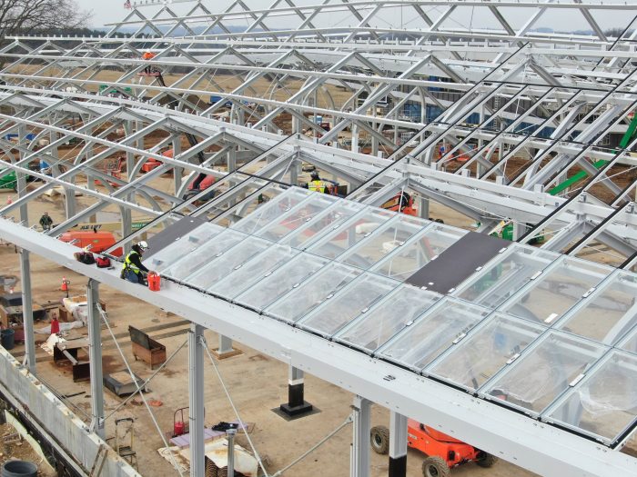 a construction worker installs large rectangular panes of glass within the framework of a large conservatory structure