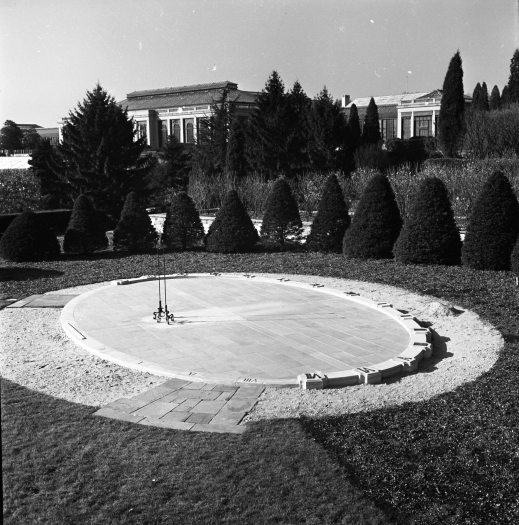 black and white photo of an oval shaped sundial in a garden