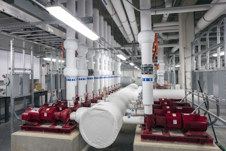 A room filled with large white and red metal machinery is seen in an underground pumproom.