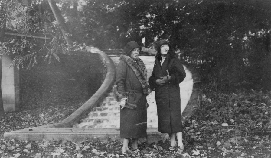 Two women stand in a garden in front of a staircase covered in water