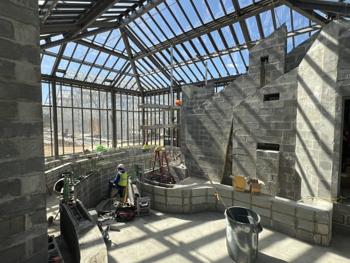 Indoor garden space under construction, featuring curving stone walls and glass roof and walls.