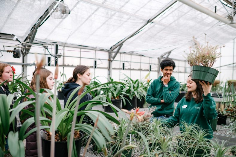 person holding up a potted plant while speaking to teens