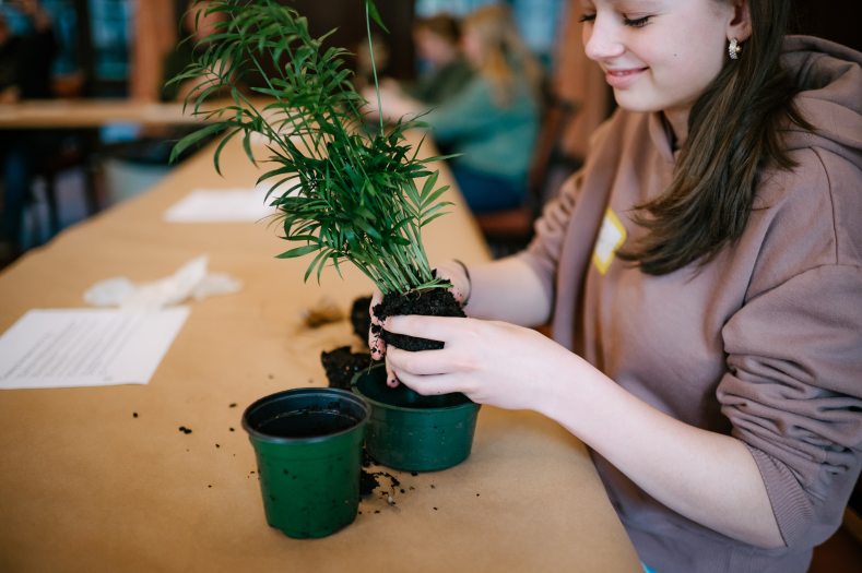 teen holding the root ball of a small  green plant with it's pot in the background