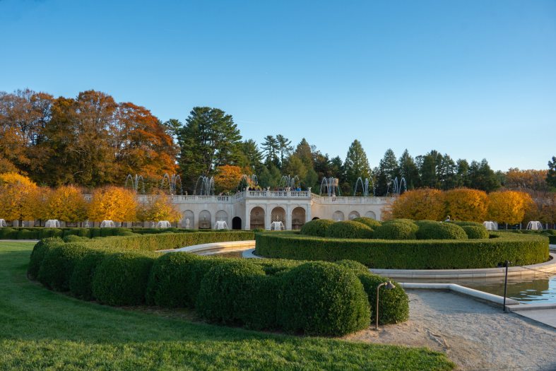The Main Fountain Garden at Longwood featuring rows of boxwood trees and fall color leaves on either side of a stone facade.