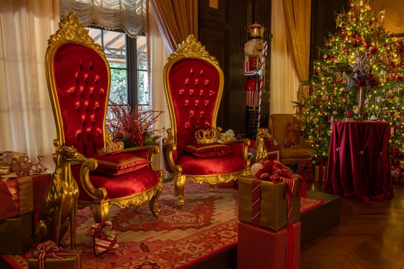 Two large red and gold thrones are flanked by lifesize brass hounds and a larger-than-lifesize nutcracker, with a lit and decorated Christmas tree to the right.