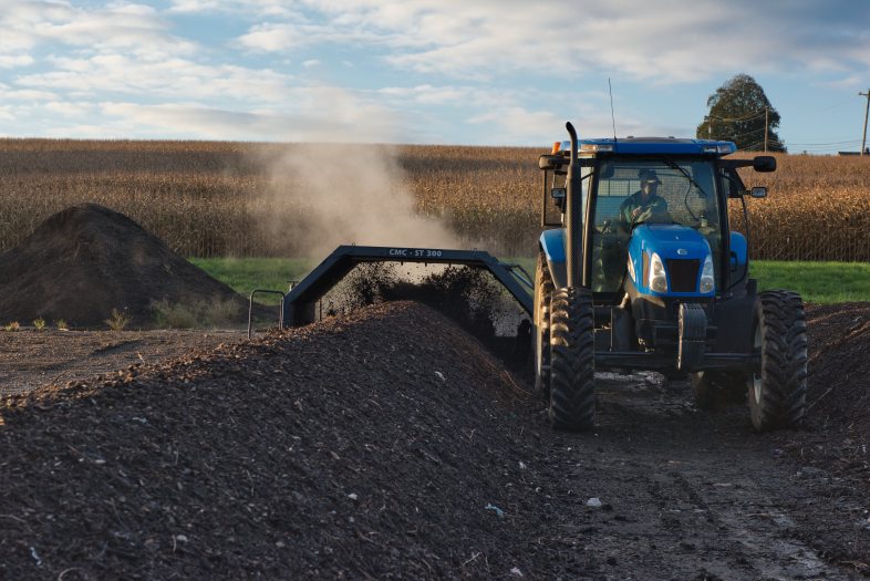 A blue tractor processes rows of compost in a green field